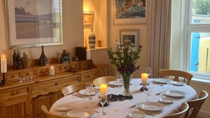A dining room with a round table set for six, wooden chairs, a vase with flowers, candles, and framed artwork on the walls. - Victorian Cottage with Garden in Tenby, Near to the Beach and Town Centre. (Tenby)