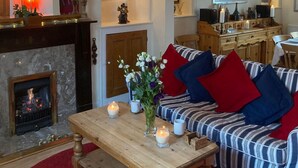 A cozy living room with a fireplace, a sofa with red and blue cushions, and a wooden coffee table. - Victorian Cottage with Garden in Tenby, Near to the Beach and Town Centre. (Tenby)