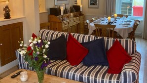A cozy living room with a striped sofa, a wooden coffee table, and a dining area with a table set for four. - Victorian Cottage with Garden in Tenby, Near to the Beach and Town Centre. (Tenby)