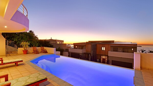 Uma área de piscina moderna com vista para o pôr do sol e o oceano.