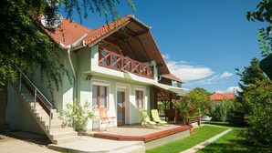 Ein zweistöckiges Haus mit roten Ziegeln auf dem Dach, einem Balkon mit hölzernen Geländern und einer Veranda mit zwei Stühlen.