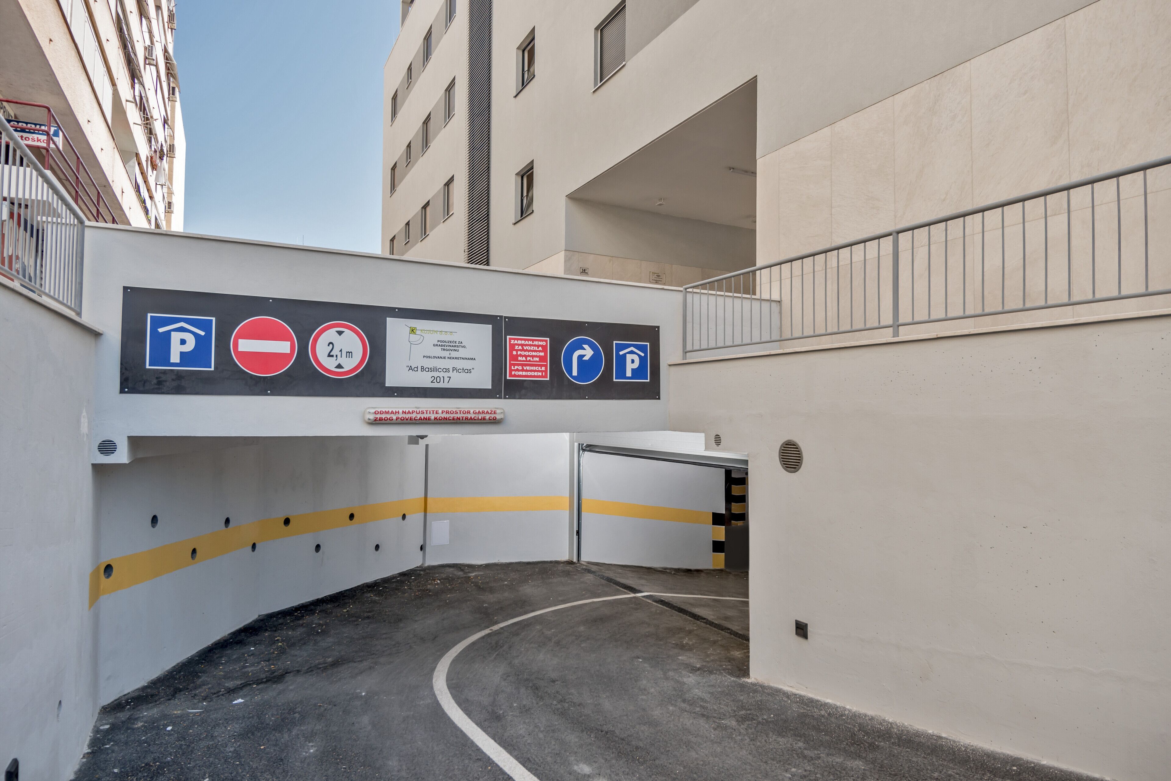 Einfahrt zu einer Parkgarage mit mehreren Schildern, die Parkregeln zeigen, und einem Hauseingang.