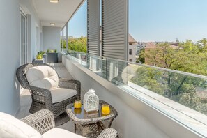 Un balcon agrémenté de meubles en osier, d’une table en verre et de deux verres de jus d’orange.