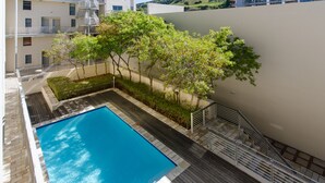 Un espace piscine aménagé sur le toit, avec une piscine à l’eau d’un bleu limpide, une terrasse en bois et un petit jardin avec des arbres.