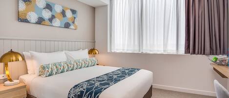 Een opgemaakt bed met een bloemenprint, een bedlampje en een kunstwerk aan de muur.