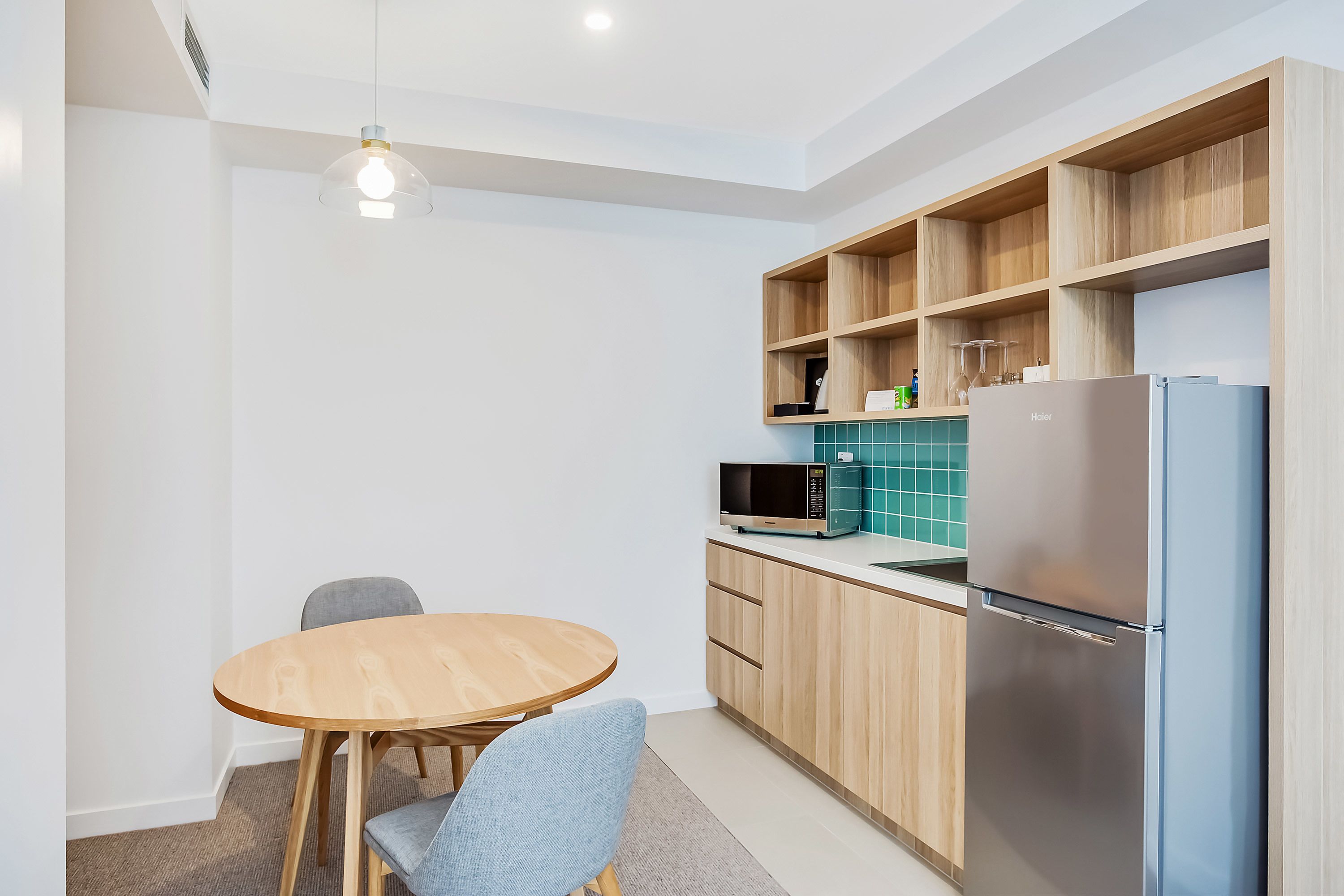 A modern kitchen with a wooden table and chairs, a built-in microwave, and a stainless steel refrigerator.