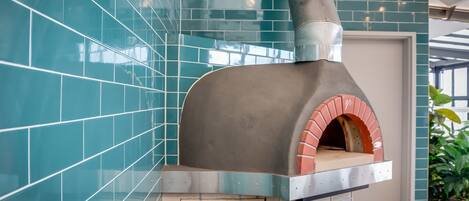 A modern kitchen with a built-in pizza oven, teal tiled walls, and a potted plant.