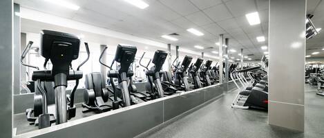A gym with multiple treadmills lined up in rows.
