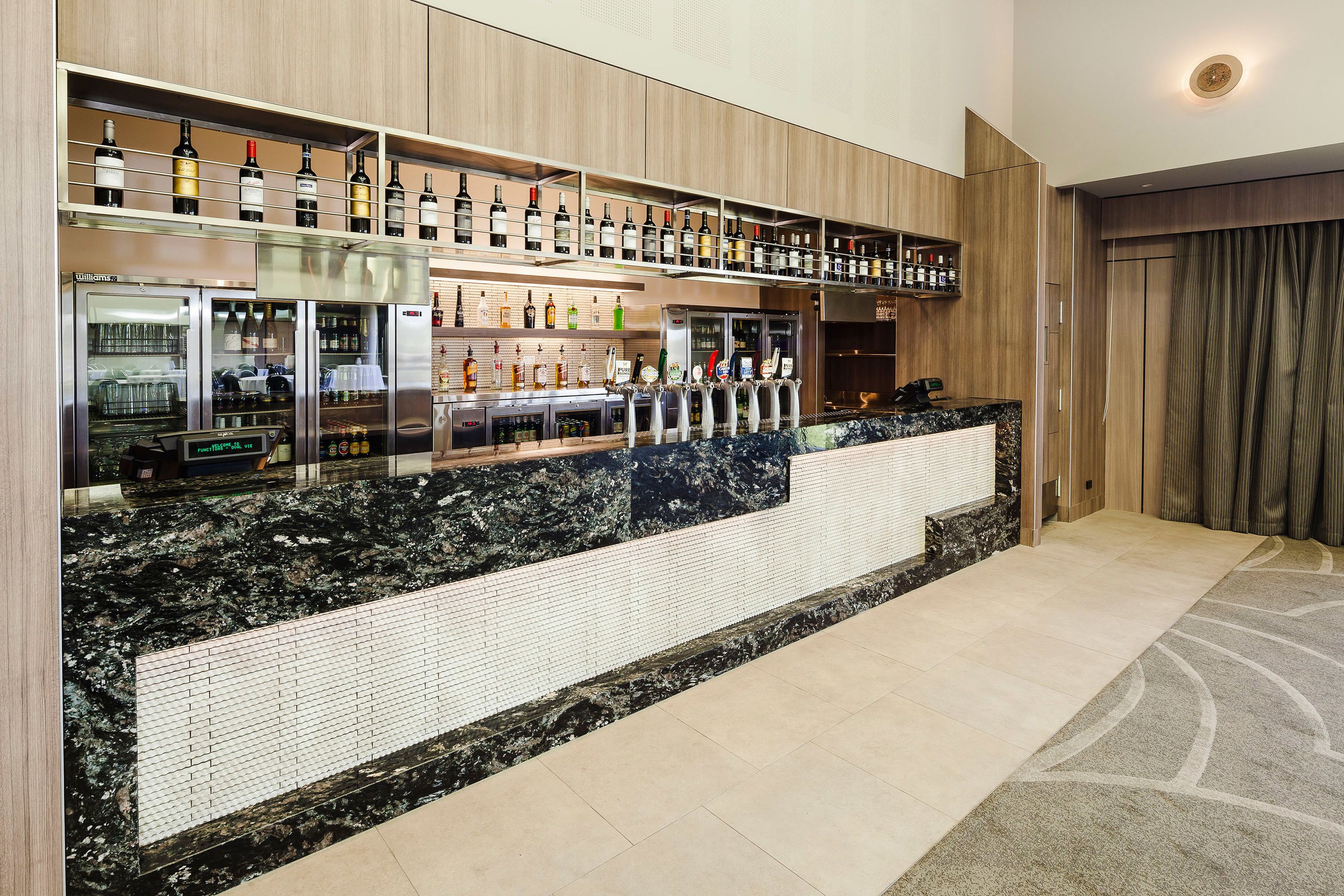 Una zona de bar moderna con encimera de mármol, botellas de vino y un expositor refrigerado.