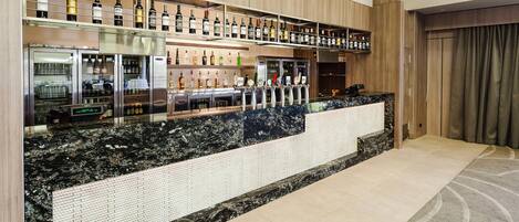 Una zona de bar moderna con encimera de mármol, botellas de vino y un expositor refrigerado.