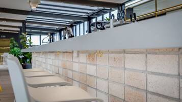 Een moderne bar met witte barstoelen, een betegelde achterwand en een plafond met zichtbare balken en hanglampen.