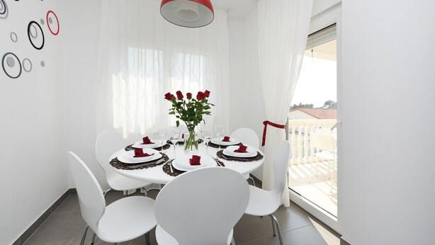 A dining area with a round table, white chairs, a vase with red roses, and a red pendant light. - Apartment Rusula Red (Zadar)