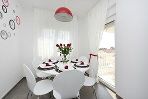 A dining area with a round table, white chairs, a vase with red roses, and a red pendant light.