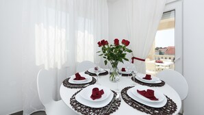 A dining area with white tables, red napkins, and a vase of red roses. - Apartment Rusula Red (Zadar)