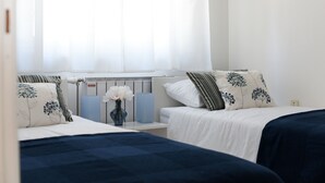A bedroom with two beds, a nightstand, a vase with flowers, and a radiator. - Apartment Rusula Red (Zadar)