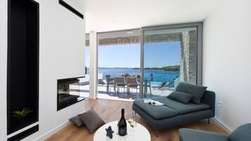 Una sala moderna con un sofá, una mesa de centro y un televisor. Cuenta con un gran ventanal que da a un balcón con vistas al mar.