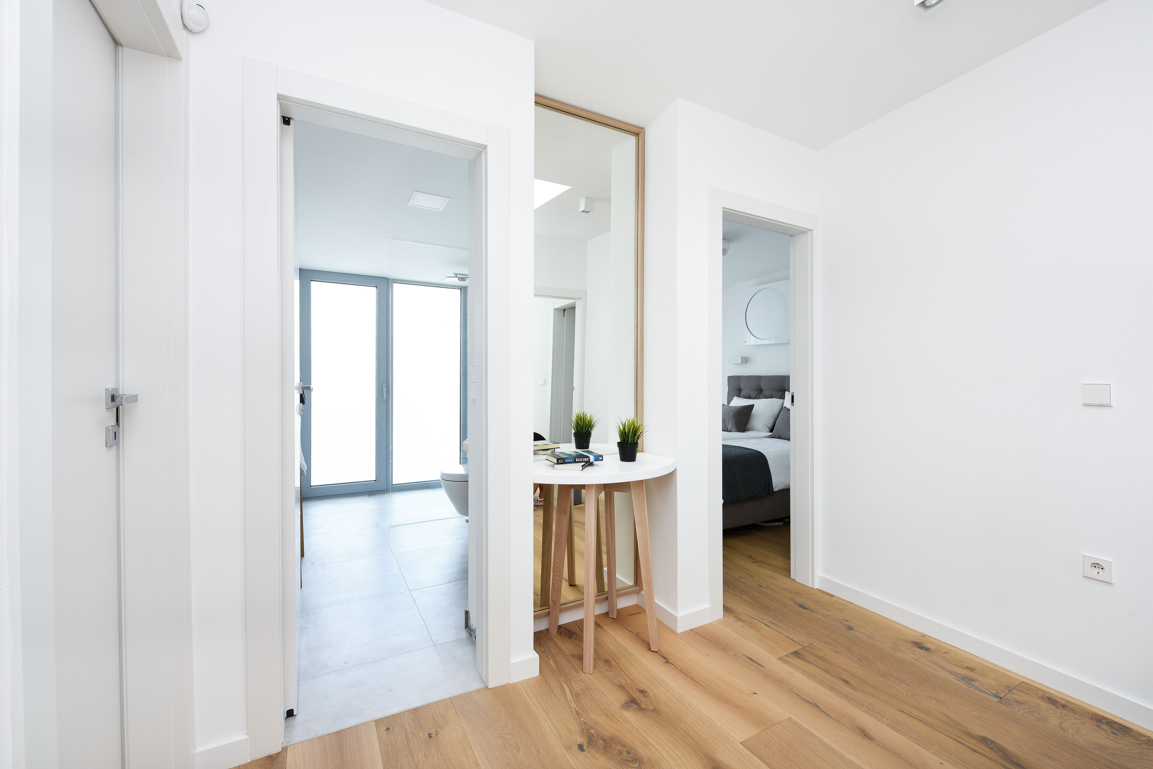 A modern interior with a wooden floor, white walls, and a round table with two potted plants.