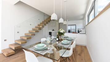 Una cocina moderna con armarios blancos, una escalera de cristal y un comedor con una mesa de cristal y sillas blancas.