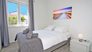 Ein Schlafzimmer mit einem Bett, einem Nachttisch, einer Lampe und einem Gemälde, das einen Sonnenuntergang über einem Steg zeigt.