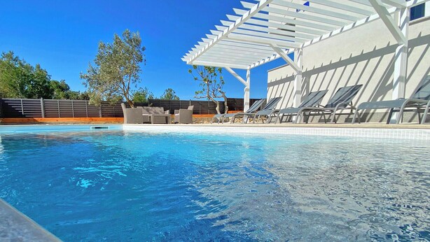 Ein Schwimmbecken mit klarem, blauem Wasser, umgeben von Liegestühlen und einer Pergola.