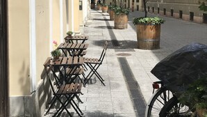 A narrow street with outdoor seating, a bicycle parked, and buildings with classical architecture. - Chestnut & Eliza Suites - Superior Homes (Budapest)