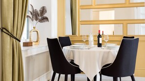 A dining area with a table set for two, a vase with decorative feathers, and a chandelier. - Chestnut & Eliza Suites - Superior Homes (Budapest)