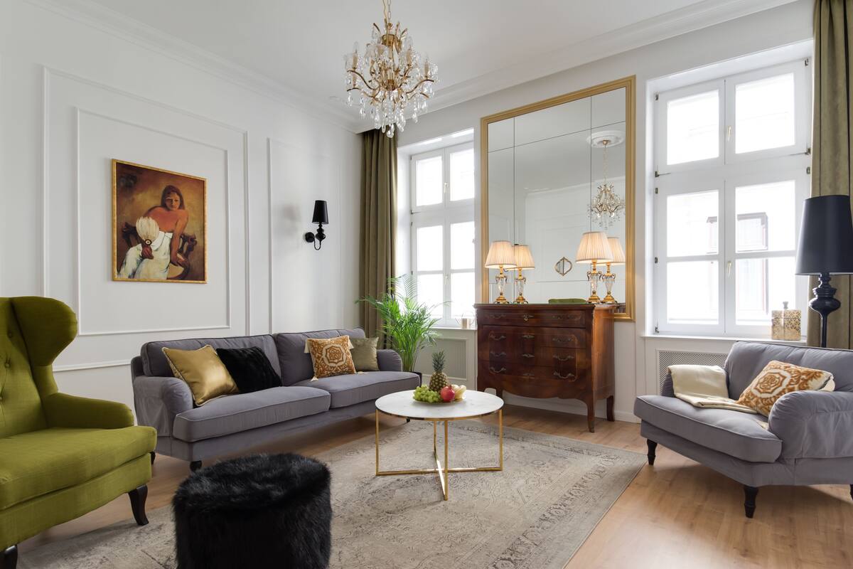 Een woonkamer met een grijze bank, een groene fauteuil, een ronde salontafel en een grote spiegel.