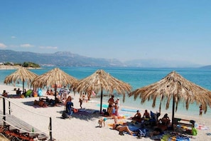 Ein Strand mit Reetdachschirmen, Liegestühlen und entspannten Menschen.