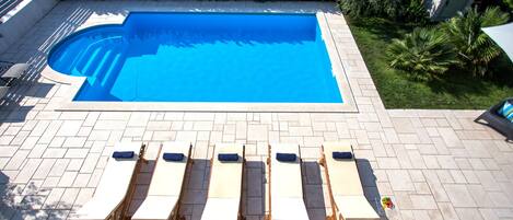 A swimming pool with a tiled deck and lounge chairs.