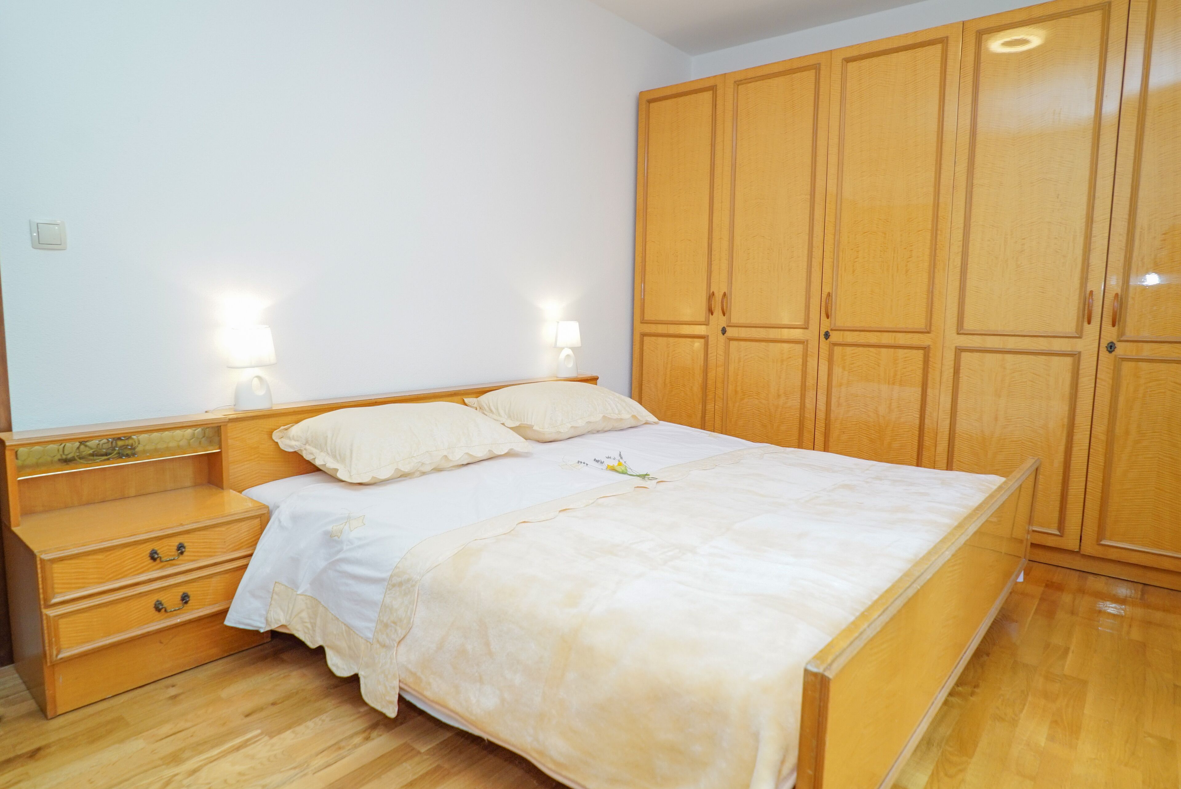 A bedroom with a wooden bed, a nightstand, a wardrobe, and two wall-mounted lamps.