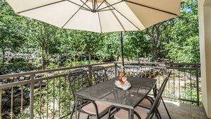 Une terrasse extérieure avec une table et des chaises, un grand parasol et une vue sur une zone boisée.