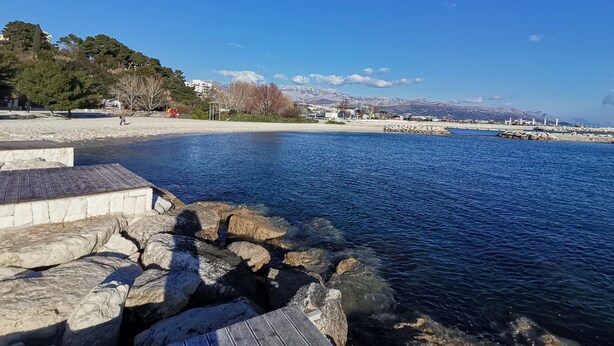 Une zone riveraine caractérisée par une côte rocheuse, une eau d’un bleu limpide et une chaîne de montagnes visible au loin.