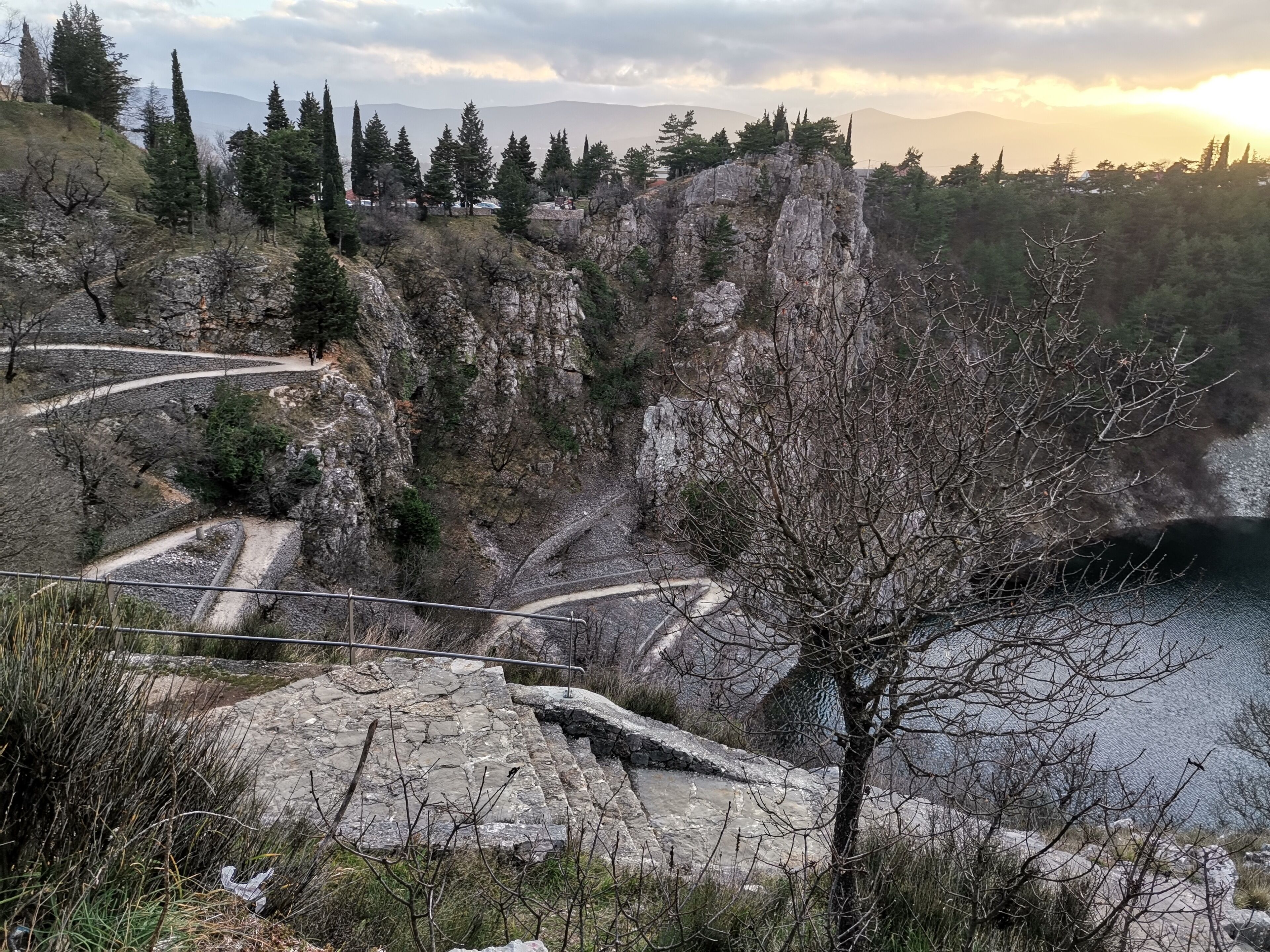 Un sendero sinuoso atraviesa un terreno rocoso con árboles dispersos y vistas a montañas distantes.