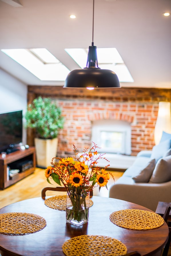 A dining area with a round table, a vase of sunflowers, and a hanging light fixture.
