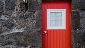 A red door with a white window, a stone wall, and a lantern above it. - Adega Velha holiday home, next to the sea and mountains, ideal for couples (Calheta de Nesquim)