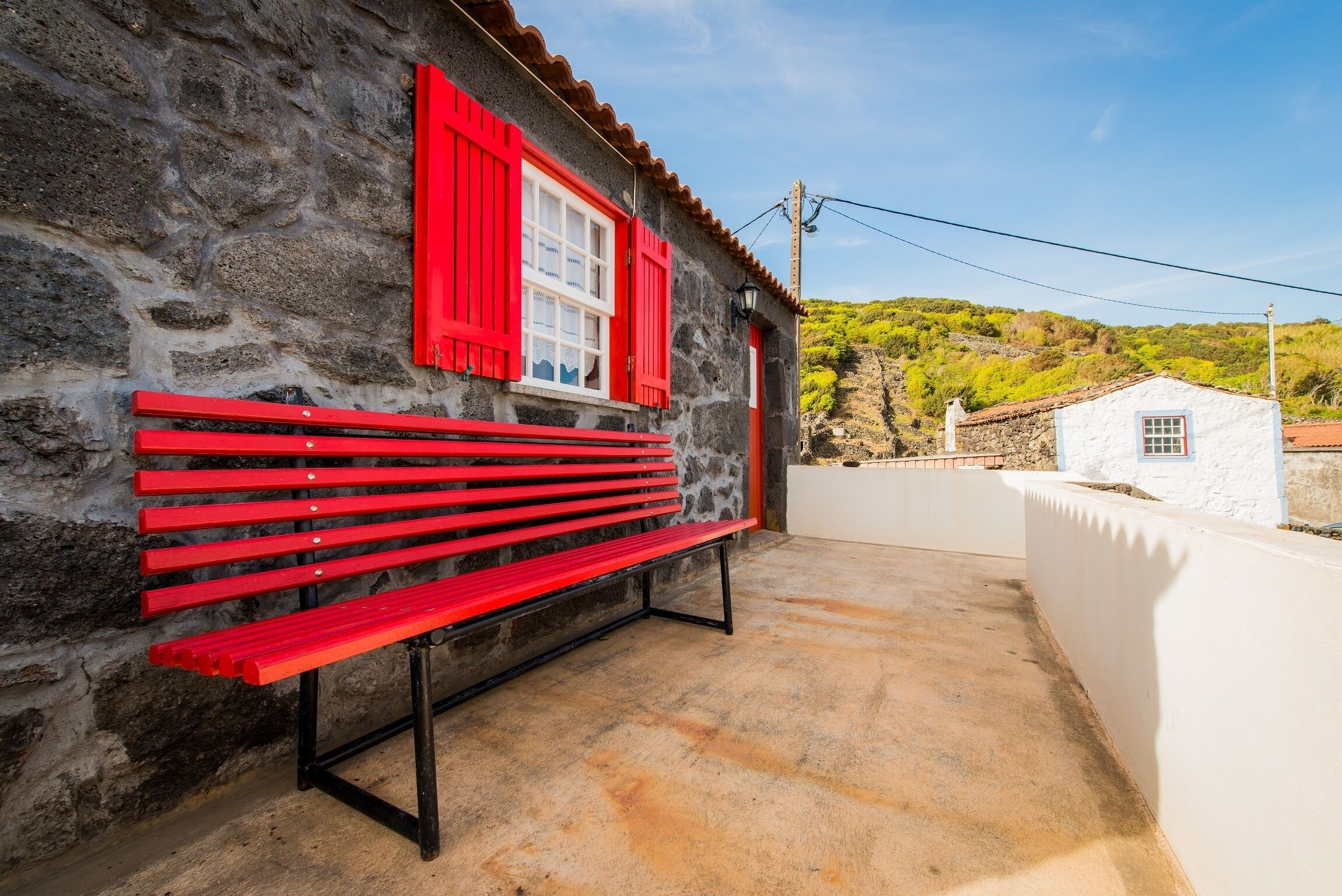 Un edificio de piedra con contraventanas rojas y una banca afuera.