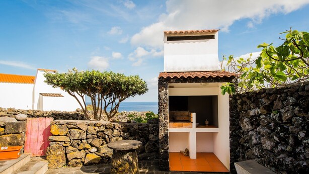A stone-walled patio with a stone table, a red gate, and a view of the sea. - Adega Velha holiday home, next to the sea and mountains, ideal for couples (Calheta de Nesquim)