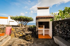 A stone-walled patio with a stone table, a red gate, and a view of the sea.