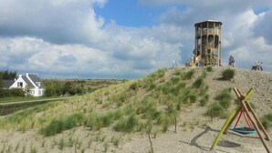 A sandy landscape with a white house and a large, unfinished structure on a hill.