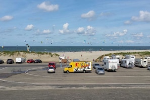 Een parkeerplaats aan het strand met campers en een gele bus met de tekst 