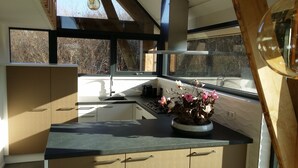 A modern kitchen with a large window, wooden beams, and a flower vase on the counter.