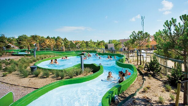 A water park with multiple pools and slides, surrounded by greenery and a clear sky.