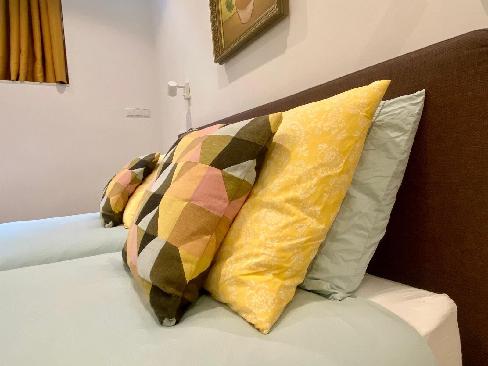 A bed with multiple pillows, a wall-mounted light, and a framed picture.