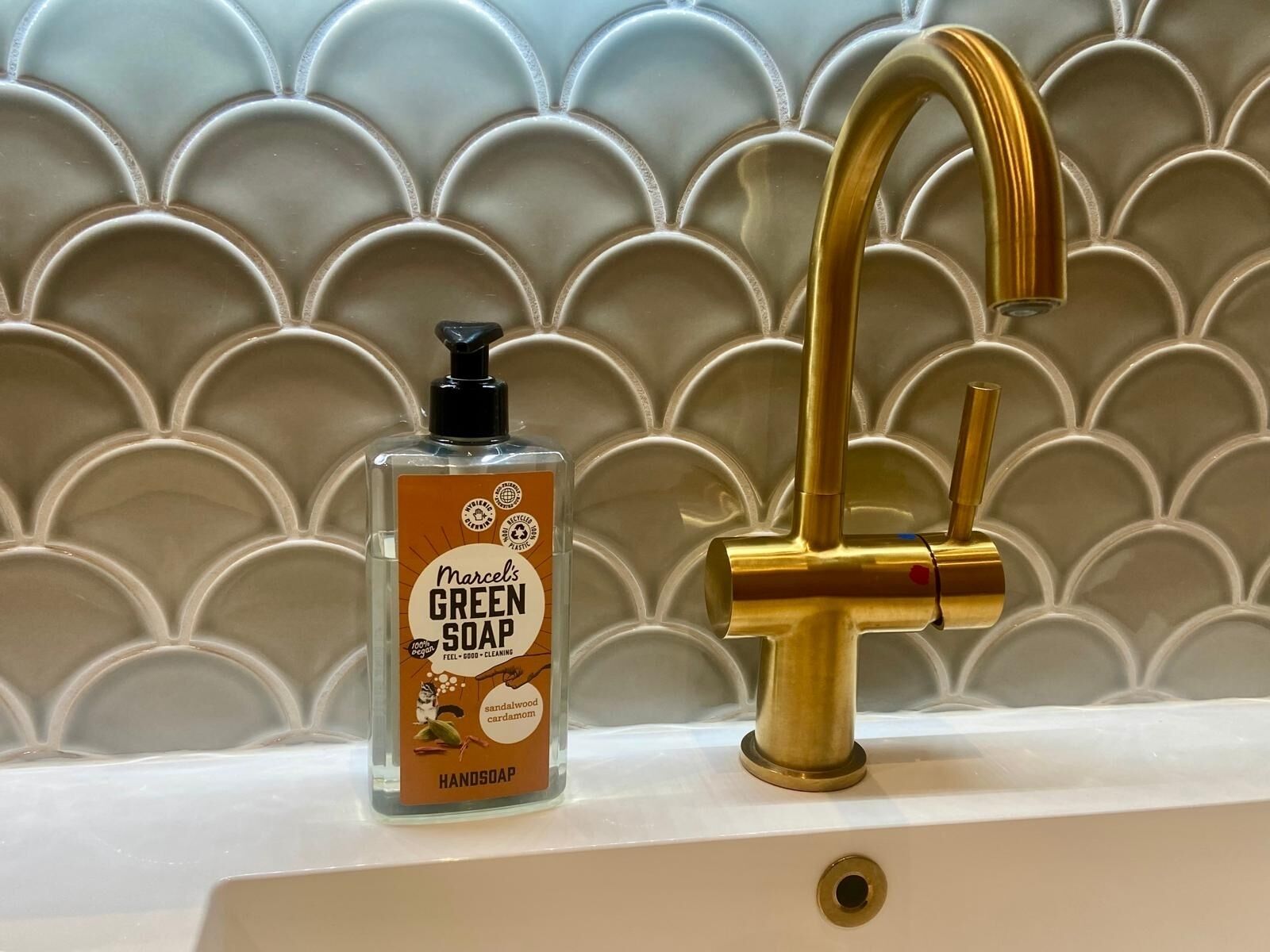 A bathroom with a gold faucet and a bottle of Marcel's Green Soap on the sink.