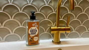 A bathroom with a gold faucet and a bottle of Marcel's Green Soap on the sink.