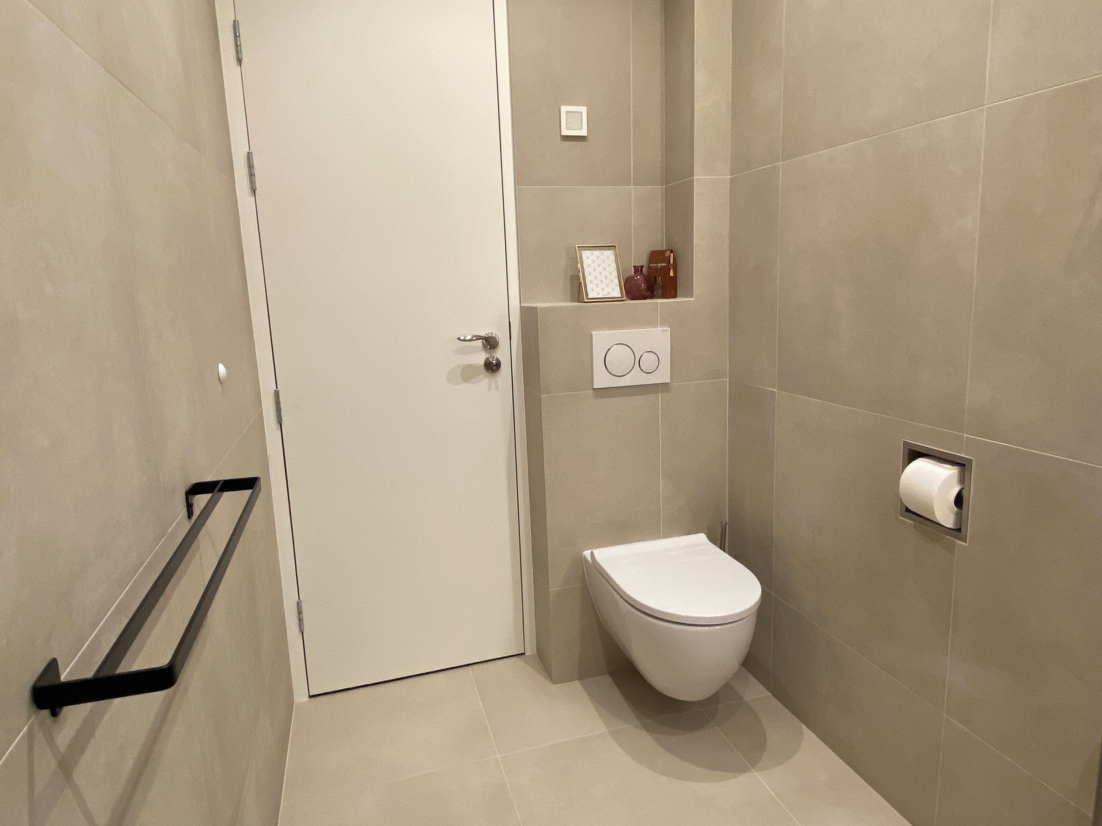 Un baño con inodoro, toallero, estante con artículos de aseo y dispensador de papel higiénico.