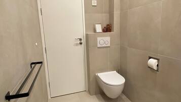 Un baño con inodoro, toallero, estante con artículos de aseo y dispensador de papel higiénico.
