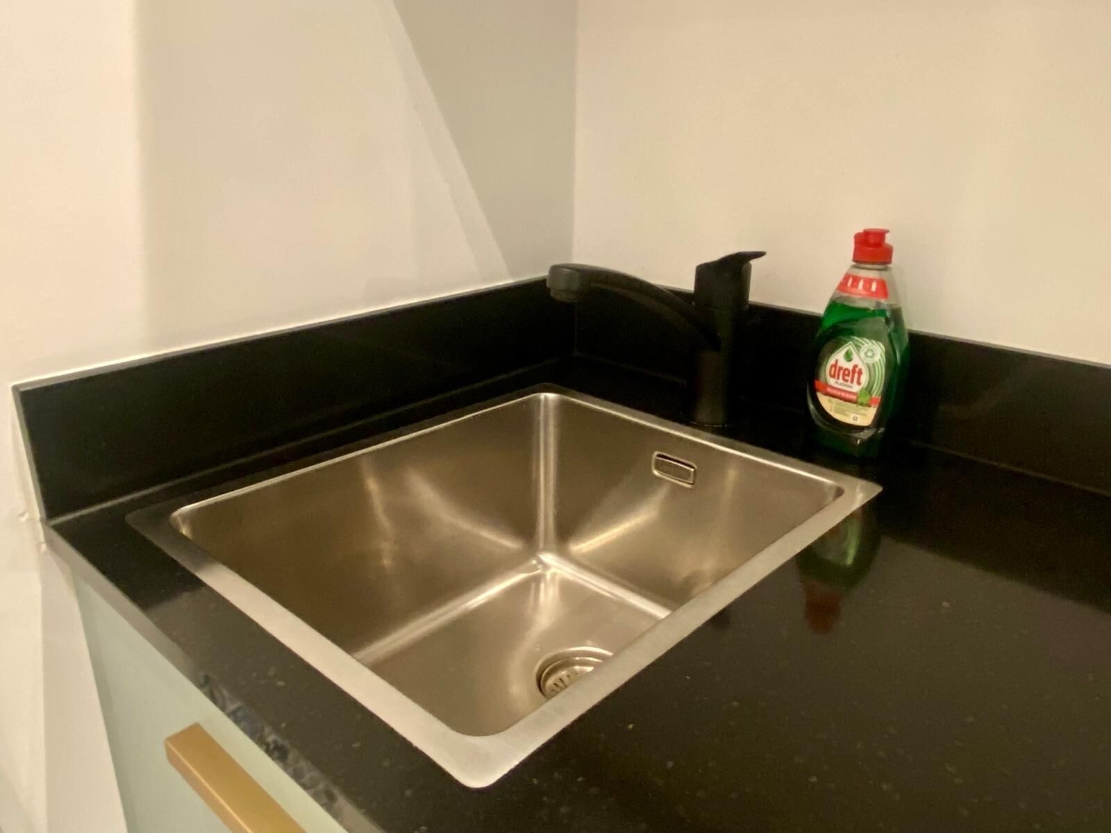 A stainless steel kitchen sink with a black countertop and a bottle of dish soap.