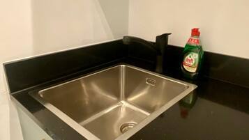 A stainless steel kitchen sink with a black countertop and a bottle of dish soap.