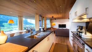 Une cuisine moderne dotée d’un grand îlot central, d’un coin repas offrant une vue agréable et d’un espace de vie avec un canapé et un téléviseur.